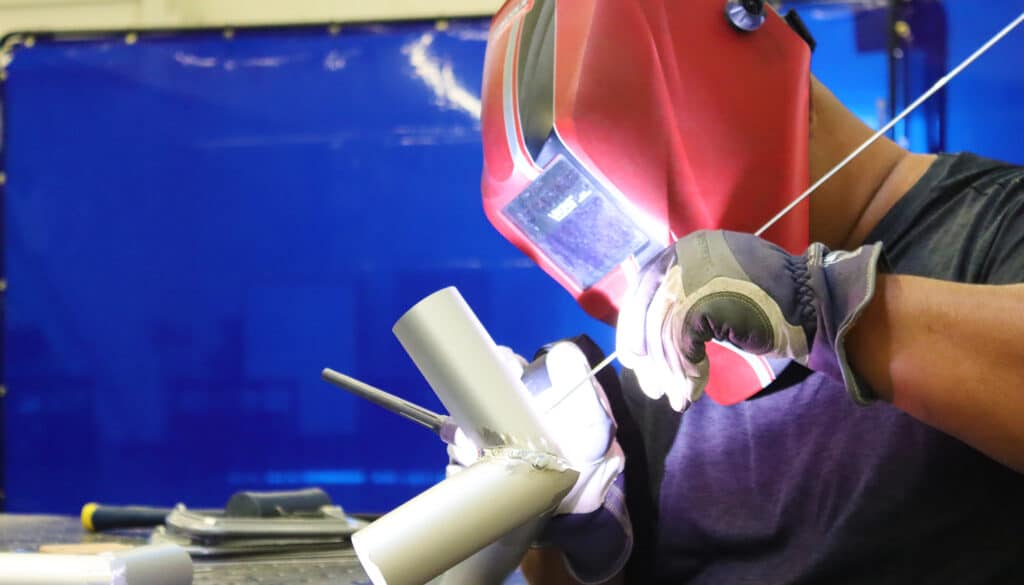 A Man welding a frame tube junction piece.