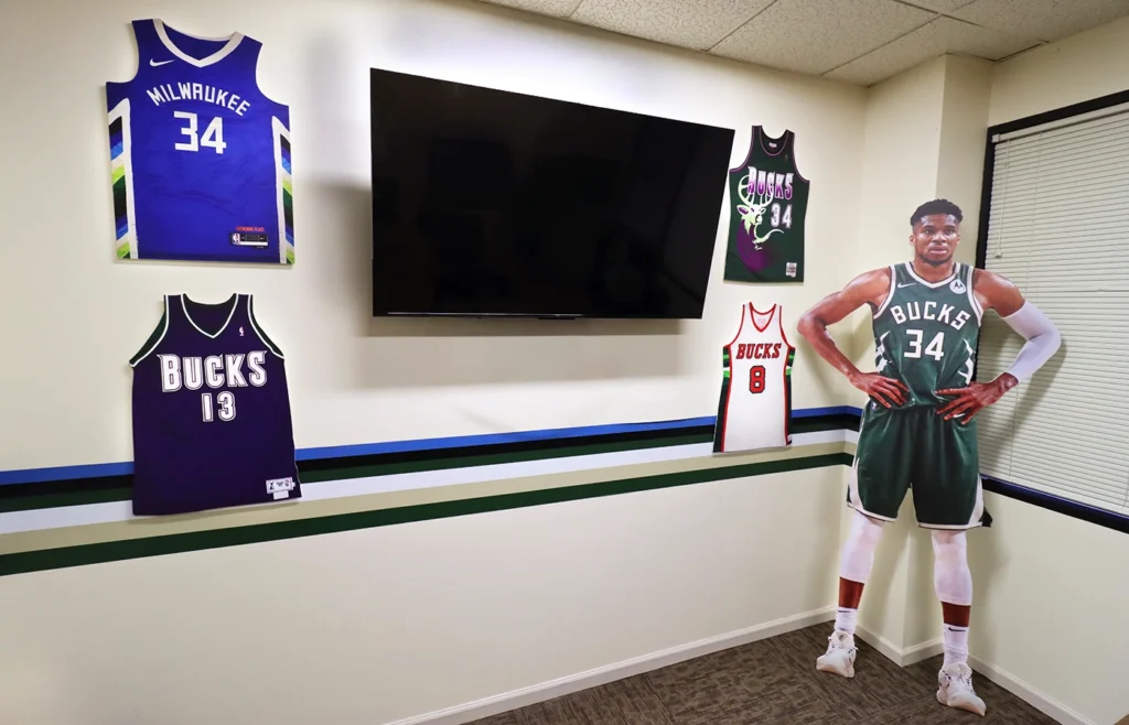 A corporate office featuring cutouts of Bucks' jerseys and Giannis Antetokounmpo on rigid boards.